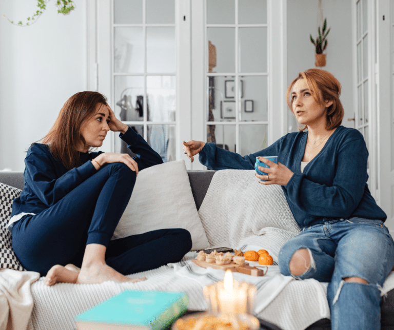 Two women sitting on a couch talking to one another.